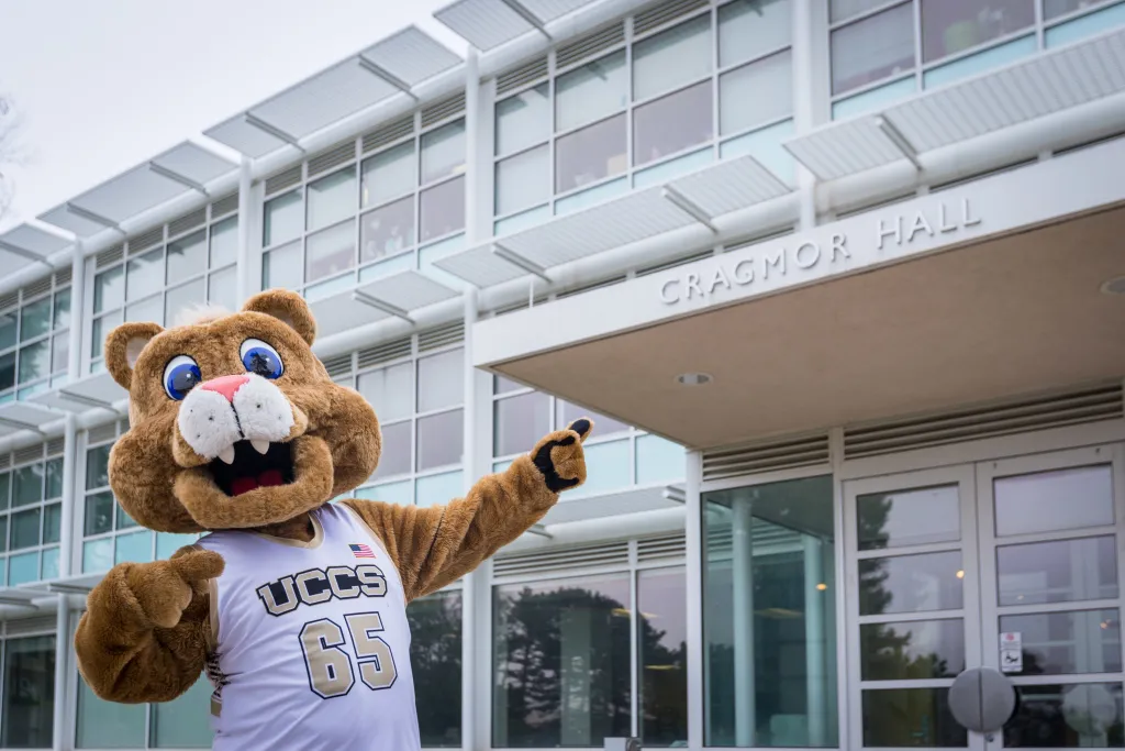 Clyde, the UCCS Mascot, pointing to the entrance to Cragmor Hall